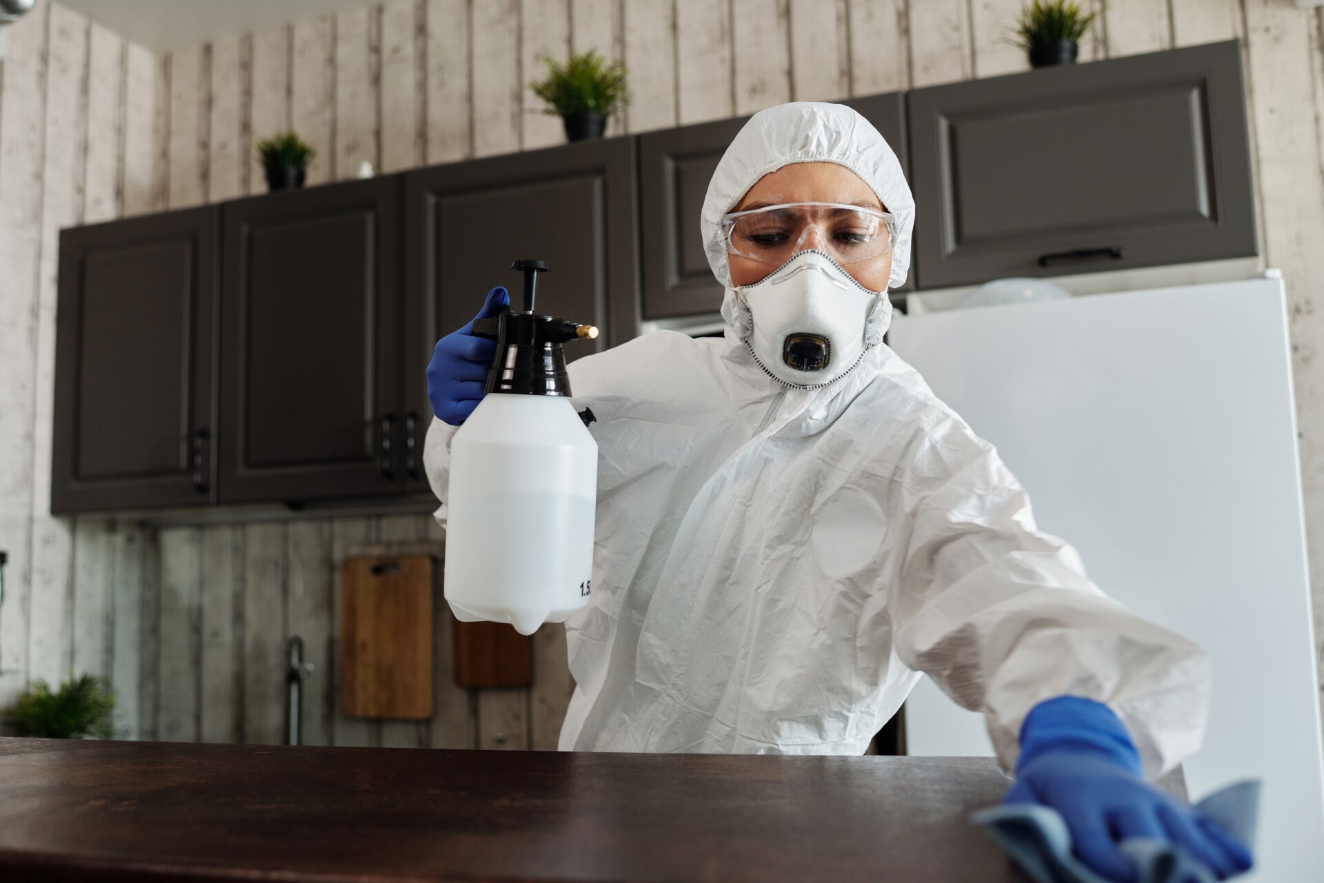 A woman wearing face mask and PPE is cleaning the table